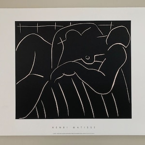 Puede incluir: Impresión en blanco y negro de una figura desnuda reclinada en un sofá a rayas. El nombre del artista, Henri Matisse, está impreso en la parte inferior de la impresión.