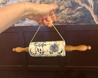 May include: A rolling pin with wooden handles and a ceramic barrel decorated with blue floral patterns. The rolling pin is suspended by a string.