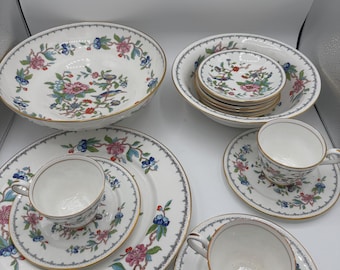 Könnte beinhalten: Eine Sammlung weißer Porzellangeschirre mit Blumen- und Vogelmotiven. Das Set umfasst Servierschalen, Teller, Untertassen und Teetassen. Die Ränder sind mit Gold und einem grauen Rand versehen. Das Blumenmuster hat rosa, blaue und grüne Akzente.