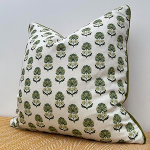 May include: A square cushion featuring a white fabric with a repeating pattern of green floral motifs. The cushion has a green border and is placed on a yellow surface.