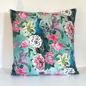 May include: A teal blue pillow with a floral and peacock design. The pillow features pink, white, and green flowers, as well as a blue peacock with green and gold feathers.