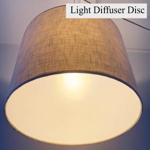 May include: A cylindrical drum lampshade with a textured tan fabric exterior and a white interior lining. The shade features a flat, circular Light Diffuser Disc at the bottom, which softens the light emitted from the central bulb inside.