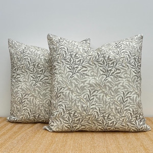 May include: Two square throw pillows with a repeating pattern of gray and white stylized leaves. The pillows are made of a soft fabric and are placed on a yellow surface. The pillows are a decorative home accessory.