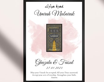 Può includere: Un download digitale stampabile di un'immagine incorniciata con uno sfondo acquerellato rosa. L'immagine presenta un'illustrazione in nero e oro della Kaaba, un edificio a forma di cubo a La Mecca, in Arabia Saudita. Il testo "Umrah Mubarak" è scritto in arabo e inglese. I nomi "Ghazala & Faisal" e la data "27.01.2023" sono anche inclusi. Il testo sotto l'immagine recita: "Che la tua Umrah sia accettata. Che tutte le tue Duas siano esaudite. Accetta i tuoi atti di adorazione. Rafforza la tua fede. Amen."