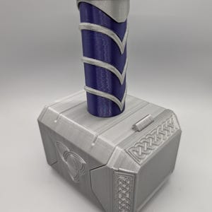 May include: A silver and blue replica of Thor's hammer, Mjolnir. The hammer features a silver head with detailed carvings and a blue handle with silver accents. A decorative item for fans of the superhero.