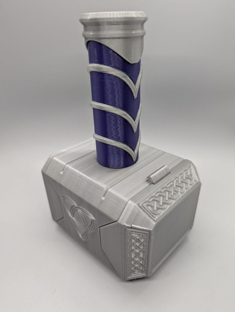 May include: A silver and blue replica of Thor's hammer, Mjolnir. The hammer features a silver head with detailed carvings and a blue handle with silver accents. A decorative item for fans of the superhero.