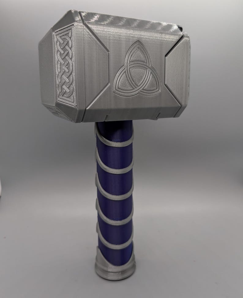 May include: A gray 3D-printed hammer with a geometric design on the head and a purple handle wrapped with silver bands. The hammer head features a Celtic knot and a braided pattern.