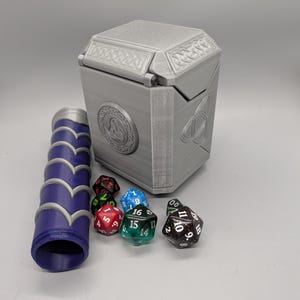 May include: A gray, 3D-printed dice box with Celtic knot and circular designs, a matching dice roller, and several multi-sided dice in various colors. The box is rectangular with a hinged lid.