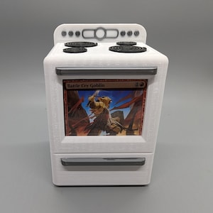 May include: A white stove with a black and red Magic: The Gathering card depicting a goblin with a sword and wings. The card is titled "Battle Cry Goblin".