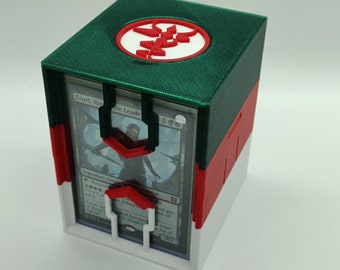 May include: A green, red, and white 3D printed card box with a black and white card inside. The box has a red and white symbol on the top. The card is titled "Ezuri, Renegade Leader".