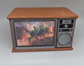 May include: A brown vintage-style television with a screen showing a fantasy illustration of a creature with a rider. The television has a silver speaker and control knobs.