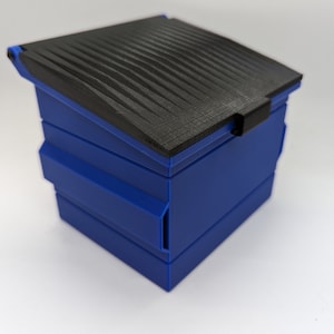 May include: A small blue plastic trash can with a black lid. The lid has a textured surface and is slightly ajar.