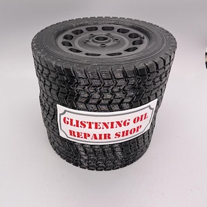 May include: A black tire with a black rim and a white sticker that says "Glistening Oil Repair Shop".