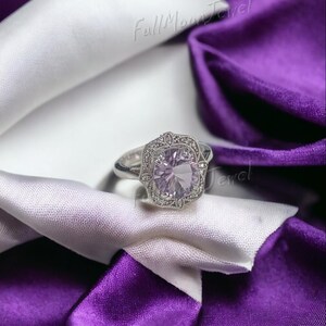 May include: A silver ring with a large, light purple gemstone at the center, surrounded by smaller clear stones. The ring is set against a backdrop of white and purple satin fabric. The text "Full Moon Jewel" is visible.