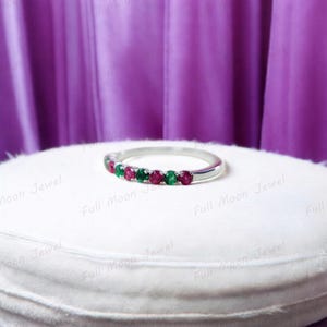 May include: A silver ring with alternating red and green gemstones. The ring is set on a white surface with a purple backdrop. The words "Full Moon Jewel" are printed on the surface.