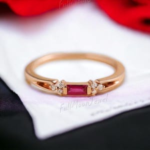 Könnte beinhalten: Roségoldener Ring mit einem rechteckigen Rubin-Mittelstein und kleinen Diamantakzenten. Der Ring hat ein zartes Band. Der Ring ist ein Schmuckstück.
