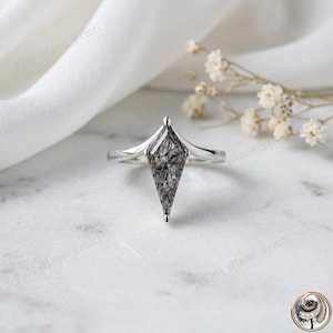 May include: A silver ring featuring a kite-shaped black and grey gemstone. The ring has a slender band and a pointed top on the gemstone. The ring is set against a white background with the text "Full Moon Jewel".