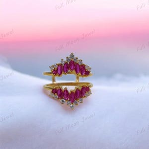 May include: A gold-colored ring with two bands, each adorned with vibrant pink marquise-cut gemstones and small white accent stones. The ring has a crown-like design, with the text "Full Moon Jewel" visible.