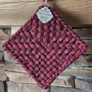 May include: A square potholder featuring a woven pattern in alternating shades of dark burgundy and muted red. A white scalloped tag is attached to the top, printed with the text Handmade by Julie's Loom, JuliesLoom.etsy.com, and Thank You!