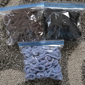 May include: Three clear plastic zip-top bags filled with shoelaces. One bag contains brown shoelaces, another contains black shoelaces, and the third contains light blue shoelaces. The shoelaces are tightly packed inside the bags.