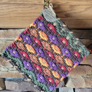 May include: A square woven potholder featuring a multi-colored geometric pattern in shades of brown, purple, orange, red, and green. A small gray tag attached with twine reads Handmade Julie's Loom, juliesloom.etsy.com, and Thank You!