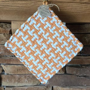 May include: A woven pot holder in orange and white, with a tag that reads "Handmade by Julie's Loom" and includes a website address and "Thank You".