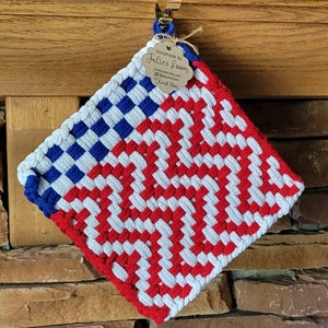 May include: Handmade woven pot holder in red, white, and blue, featuring a flag-like design. The top left corner has a blue and white checkered pattern. A small tag reads "Handmade by Julies Loom".