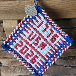 May include: A handmade, square pot holder with a woven design in red, white, and blue. The pot holder is hanging from a hook. The tag reads "Handmade by Julie's Loom".