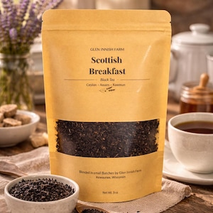 May include: A kraft paper bag of Scottish Breakfast black tea with a clear window showing the loose tea leaves. The bag has text that reads "Glen Innish Farm" and "Scottish Breakfast". A small bowl of tea leaves and a cup of tea are also visible.