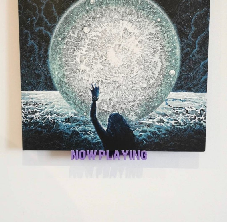 May include: A black and white illustration of a person reaching up towards a large, white, textured orb. The orb is surrounded by a dark, swirling background. The text "NOW PLAYING" is displayed below the image.