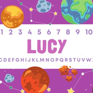 Może przedstawiać: Fioletowe tło z planetami, gwiazdami i konstelacjami. Imię "LUCY" jest dużymi r&oacute;żowymi literami, z cyframi 1-10 i alfabetem powyżej i poniżej. Projekt ma motyw kosmiczny.