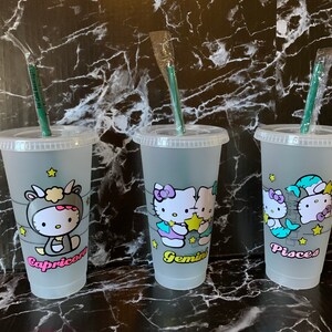 May include: Three clear plastic cups with green straws and Hello Kitty designs. Each cup features a different zodiac sign: Capricorn, Gemini, and Pisces.