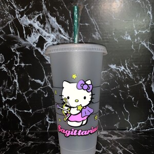 May include: A gray reusable cup with a Hello Kitty design featuring Sagittarius. The cup has a green straw and a white lid. The Hello Kitty character is wearing a pink dress and purple wings with a bow on her head. The word "Sagittarius" is written in black below the character.