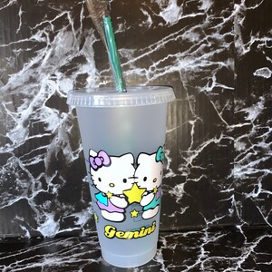 May include: A frosted clear plastic reusable cup with a lid and a green straw. The cup has a graphic of two Hello Kitty characters holding a yellow star with the word "Gemini" printed below them.