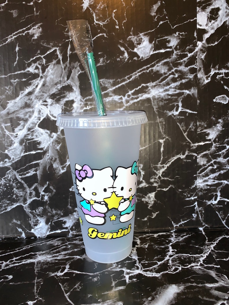 May include: A frosted clear plastic reusable cup with a lid and a green straw. The cup has a graphic of two Hello Kitty characters holding a yellow star with the word "Gemini" printed below them.