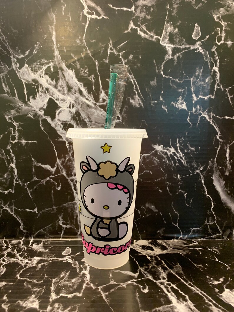 May include: White reusable cup with a Hello Kitty design. The design features Hello Kitty dressed as a Capricorn with a pink star on the cup.