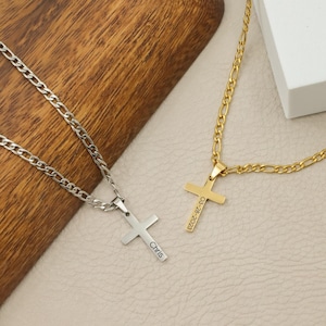 May include: Two cross necklaces. One is silver-colored with the name "Chris" engraved on the cross. The other is gold-colored with the date "03-28-2023" engraved on the cross. Both necklaces are on a light-colored surface.