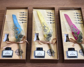 Peut inclure: Trois ensembles de stylos de calligraphie dans des boîtes-cadeaux. Chaque ensemble comprend un flacon d'encre noire, un stylo plume avec un motif d'engrenage métallique et cinq pointes. Les plumes sont bleues, jaunes et roses.