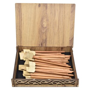 May include: A wooden box with a carved design on the front, containing a set of wooden calligraphy pens with a natural finish.
