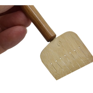 May include: A wooden tool with a handle and a flat, rectangular head with a row of small holes. The head is labeled "4.0".