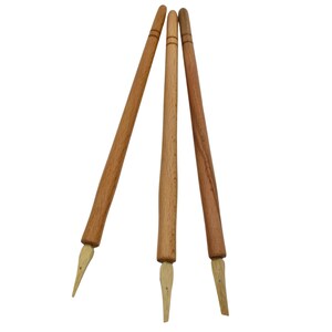 May include: Three wooden calligraphy pens with pointed tips. The pens are brown and have a natural wood finish.