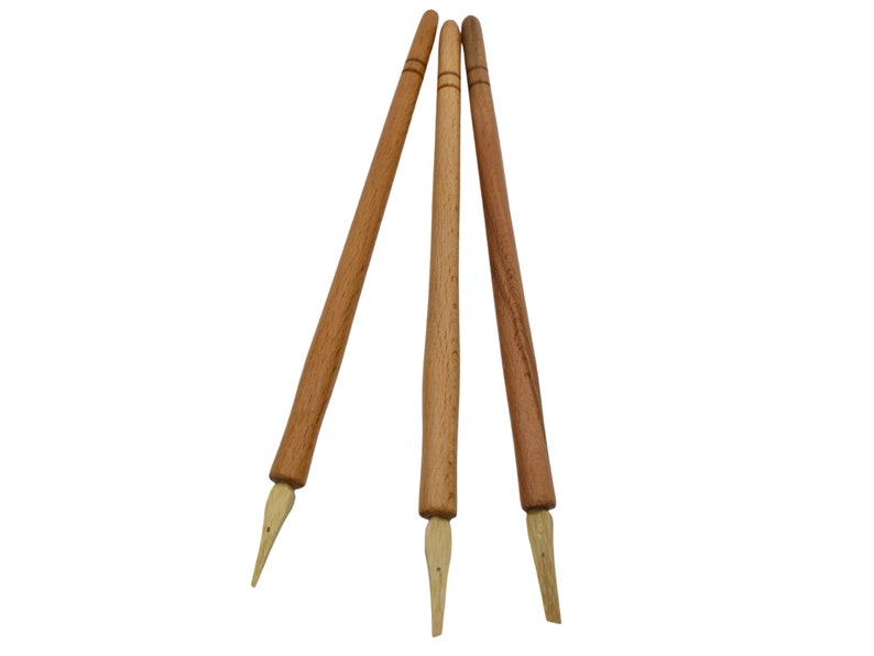 May include: Three wooden calligraphy pens with pointed tips. The pens are brown and have a natural wood finish.