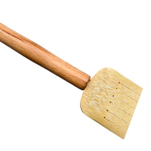 May include: A wooden tea whisk with a long handle and a flat, rectangular head with holes. The whisk is made of natural bamboo.