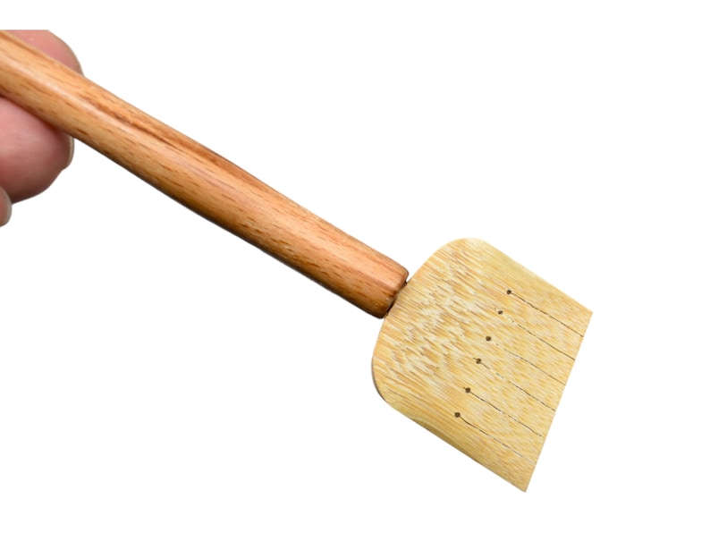 May include: A wooden tea whisk with a long handle and a flat, rectangular head with holes. The whisk is made of natural bamboo.