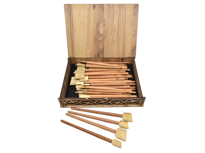 May include: A wooden box with a carved design on the lid, containing a set of 20 wooden calligraphy brushes with natural bristles. The box is open and the brushes are arranged neatly inside. Five additional brushes are shown outside the box.