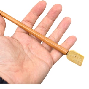 May include: A wooden calligraphy brush with a long, thin handle and a flat, rectangular brush head. The brush head is made of bamboo and has several small holes.