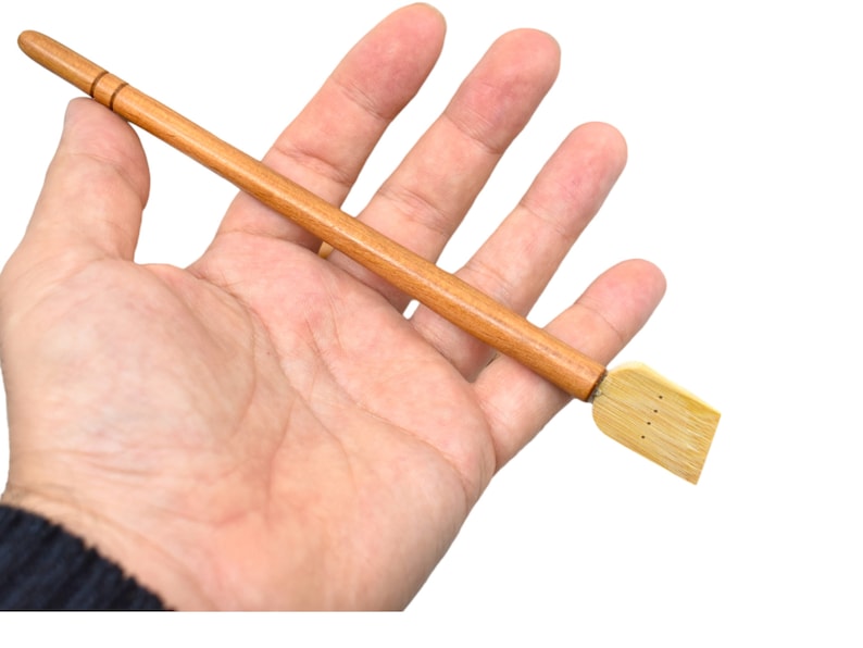 May include: A wooden calligraphy brush with a long, thin handle and a flat, rectangular brush head. The brush head is made of bamboo and has several small holes.