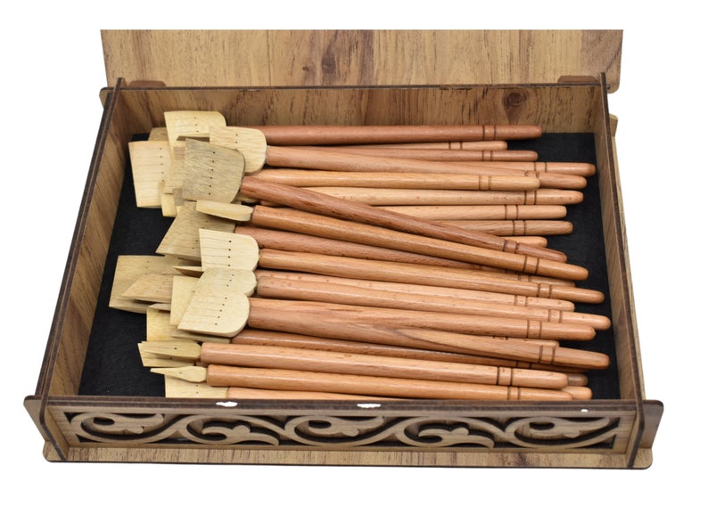 May include: A wooden box filled with a set of calligraphy pens. The pens have wooden handles and a variety of nibs. The box has a decorative design on the front.