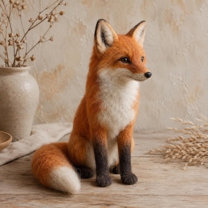 May include: A needle-felted fox figurine featuring a vibrant orange coat, a white chest and muzzle, and dark brown lower legs. The fox is depicted in a seated position with its bushy tail curled forward, showcasing a white tip and realistic black-tipped ears.