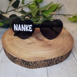 May include: Black heart-shaped sunglasses with the name "NANKE" printed in white on the left lens.